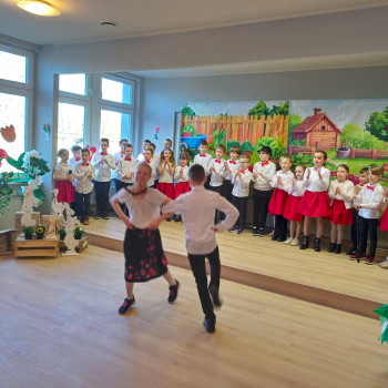 Chłopiac z dziewczynką tańcza. W tle grupa uczniow w strojach ludowych