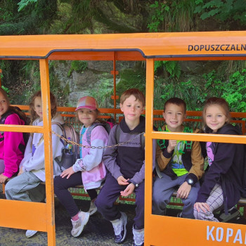 Zdjęcie grupy dzieci w pomarańczowym wagoniku z napisem kopalnia złota