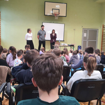 Zdjęcie szerszego planu Uczniowie siedzący na widowni w oddali odbywająca się prezentacja